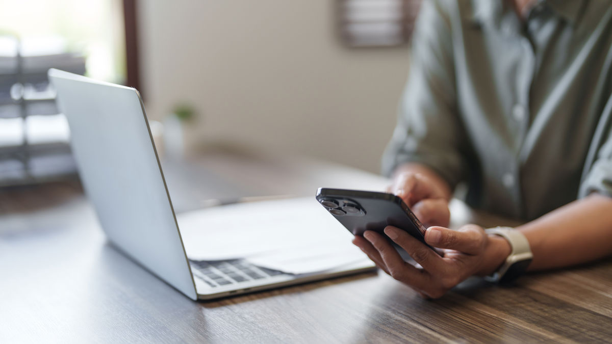 a person holding a phone and looking at a laptop