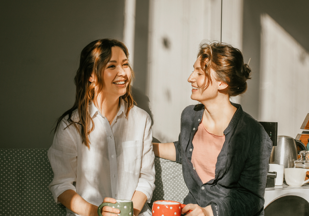 two women sitting on a bench with cups of coffee