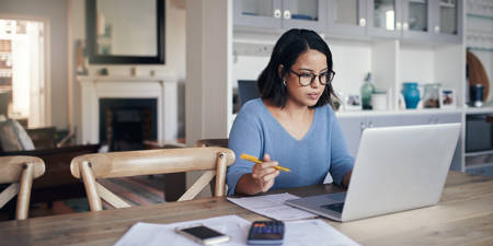Woman planning financial goals for the new year using laptop and paperwork at home